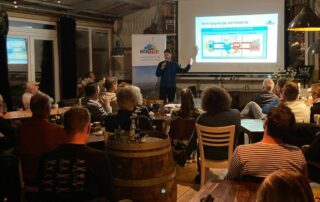 presentator staat voor scherm met presentatie over de warmtepomp met publiek