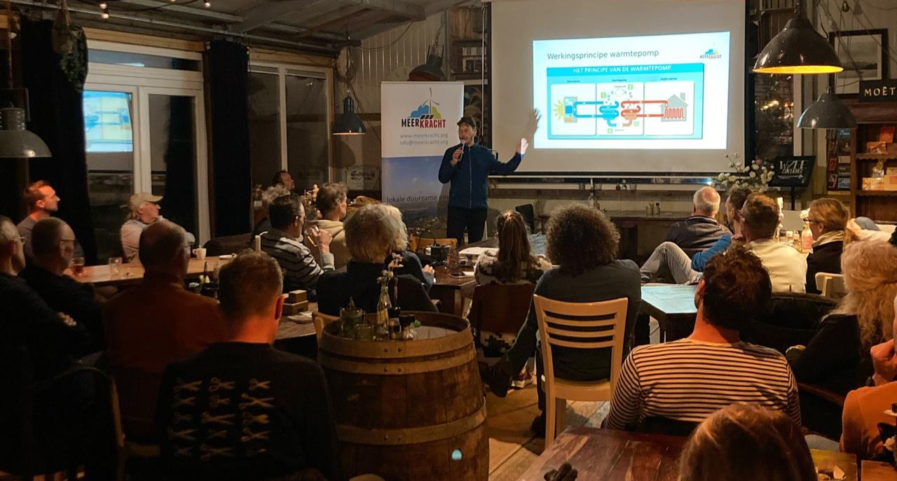 presentator staat voor scherm met presentatie over de warmtepomp met publiek